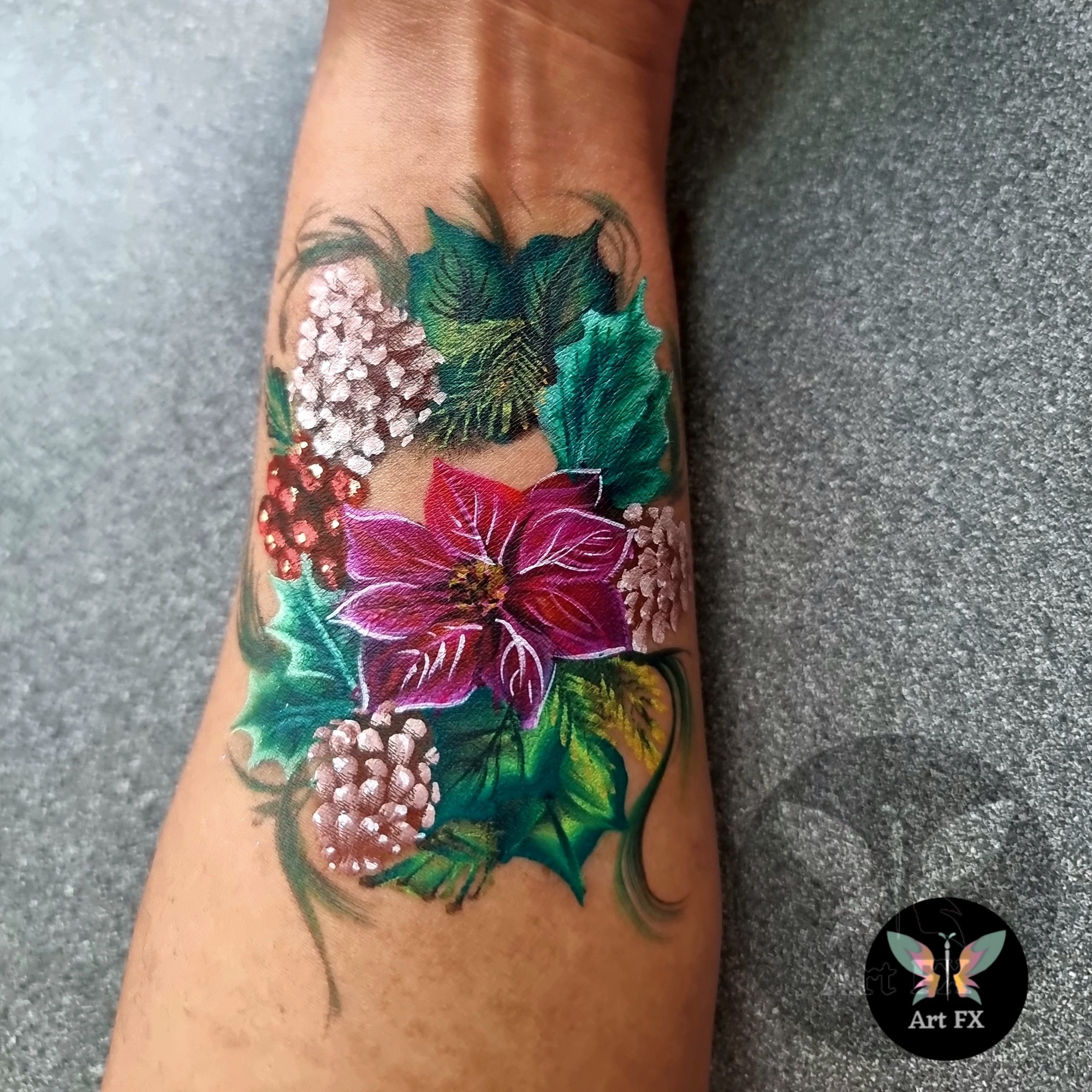 Poinsettia and winter foliage (pine cones, holly) body paint on an arm.
