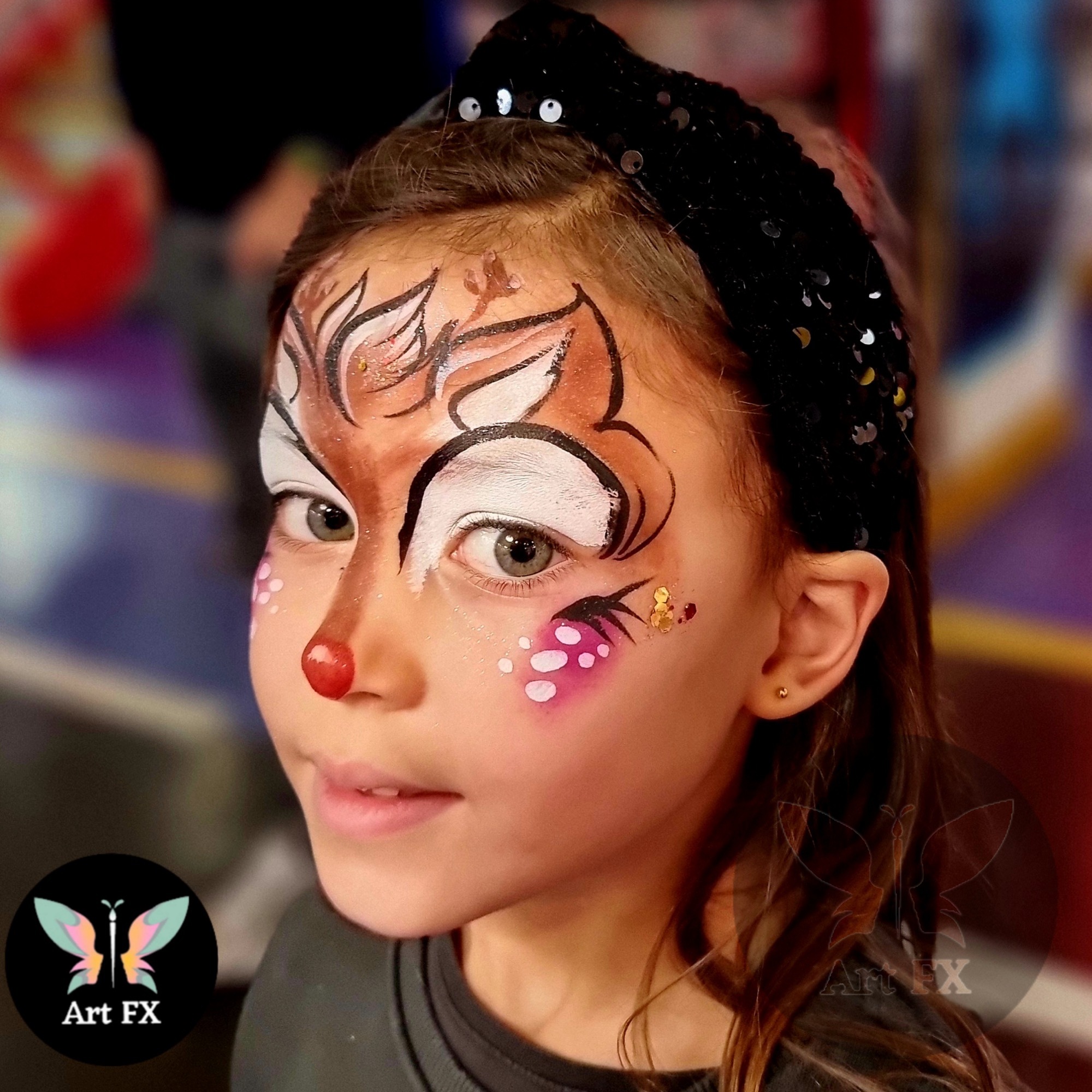 Reindeer face paint on a girl with a red nose and white dots.