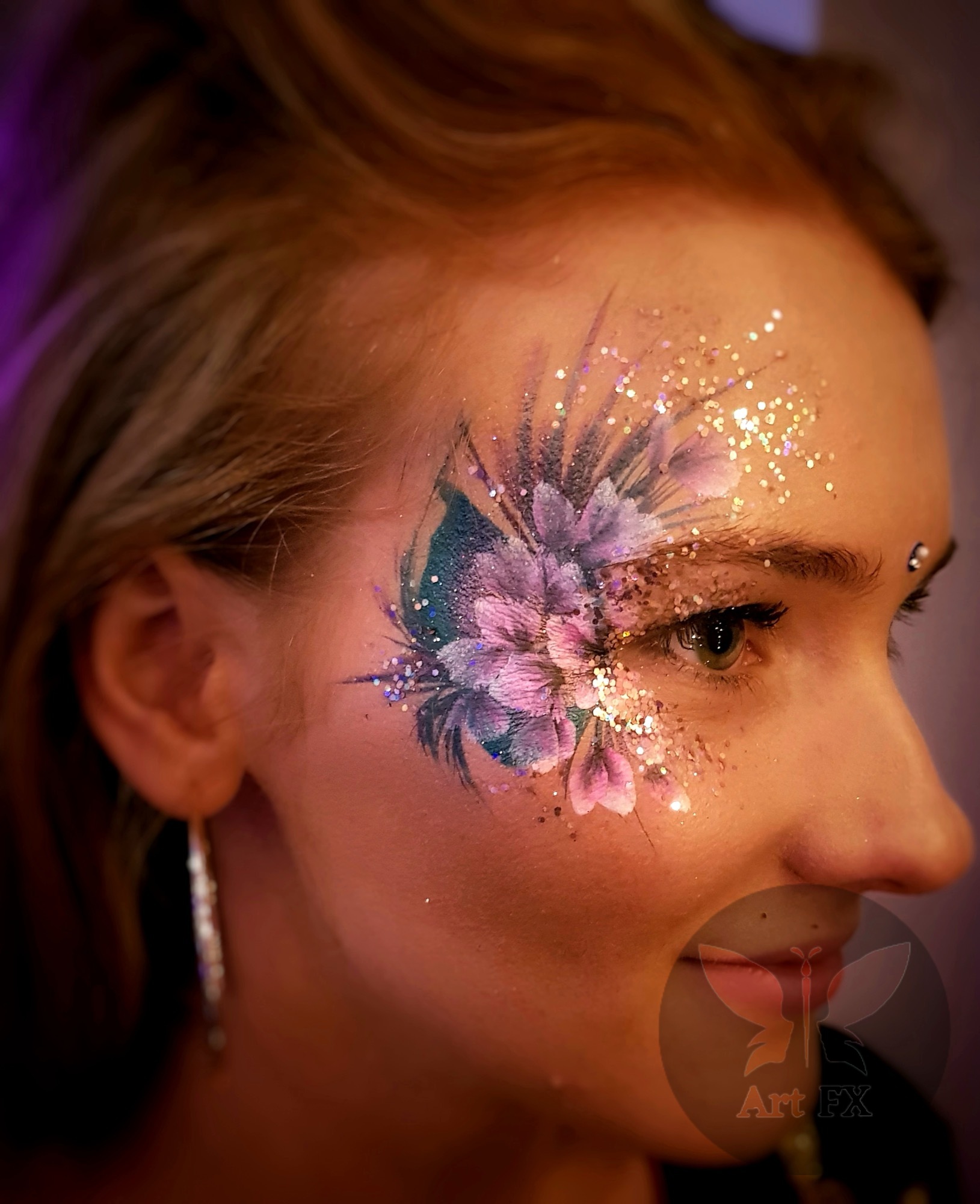 A woman with an intricate orange and yellow floral face paint design adorned with gold glitter.