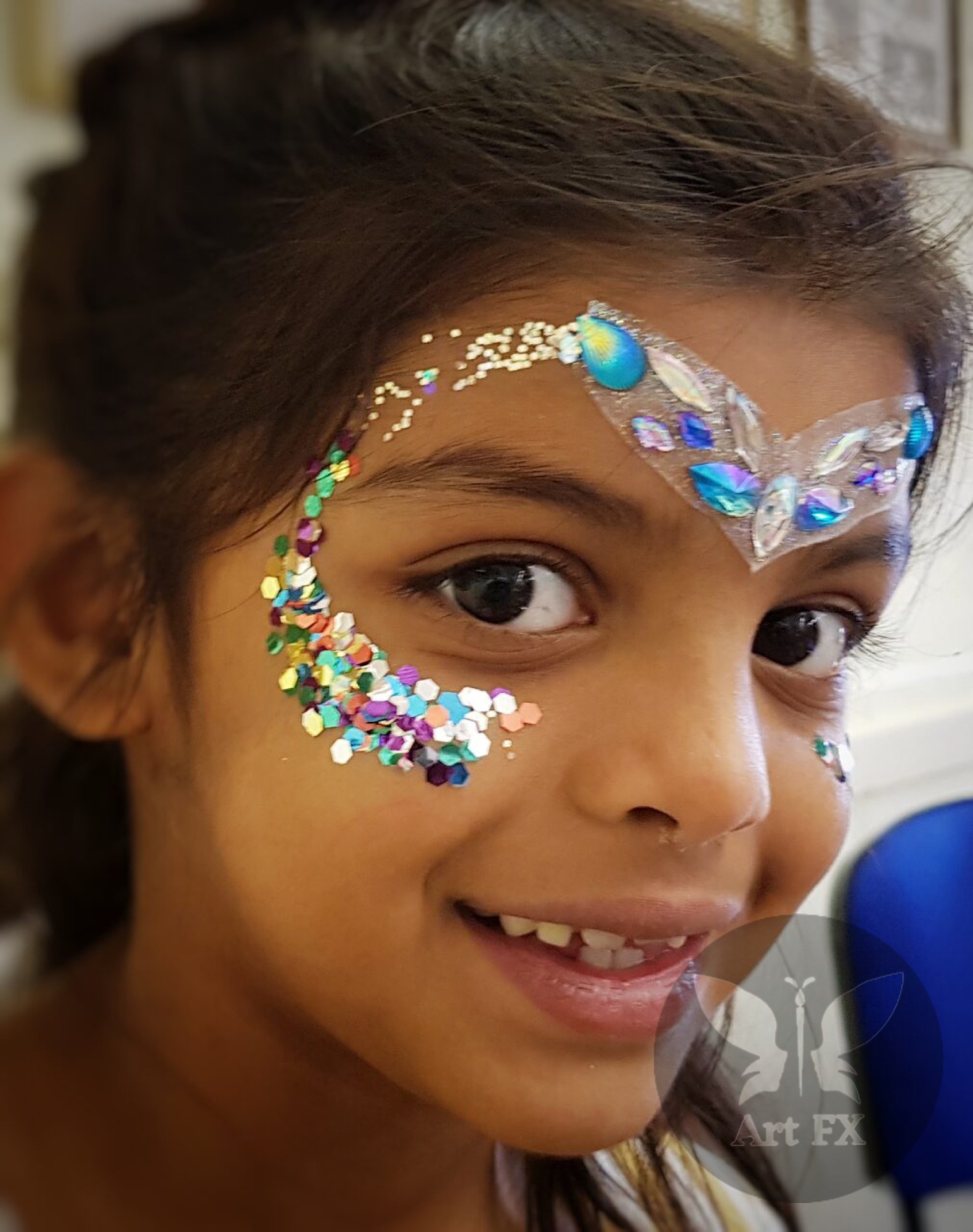 Two women at a festival, both wearing intricate pink and white floral face paint designs with sparkly glitter.