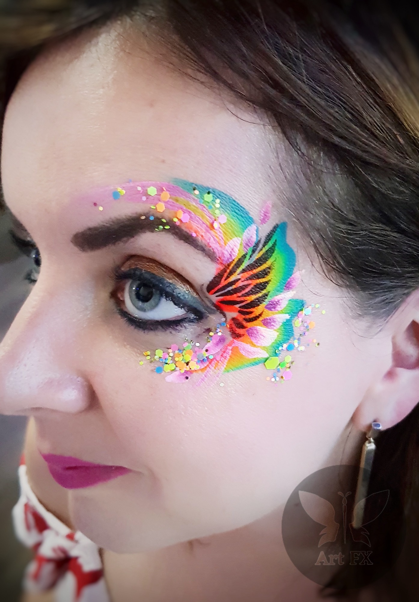 A woman displaying a lovely blue and white floral face paint design accented with matching blue chunky glitter.