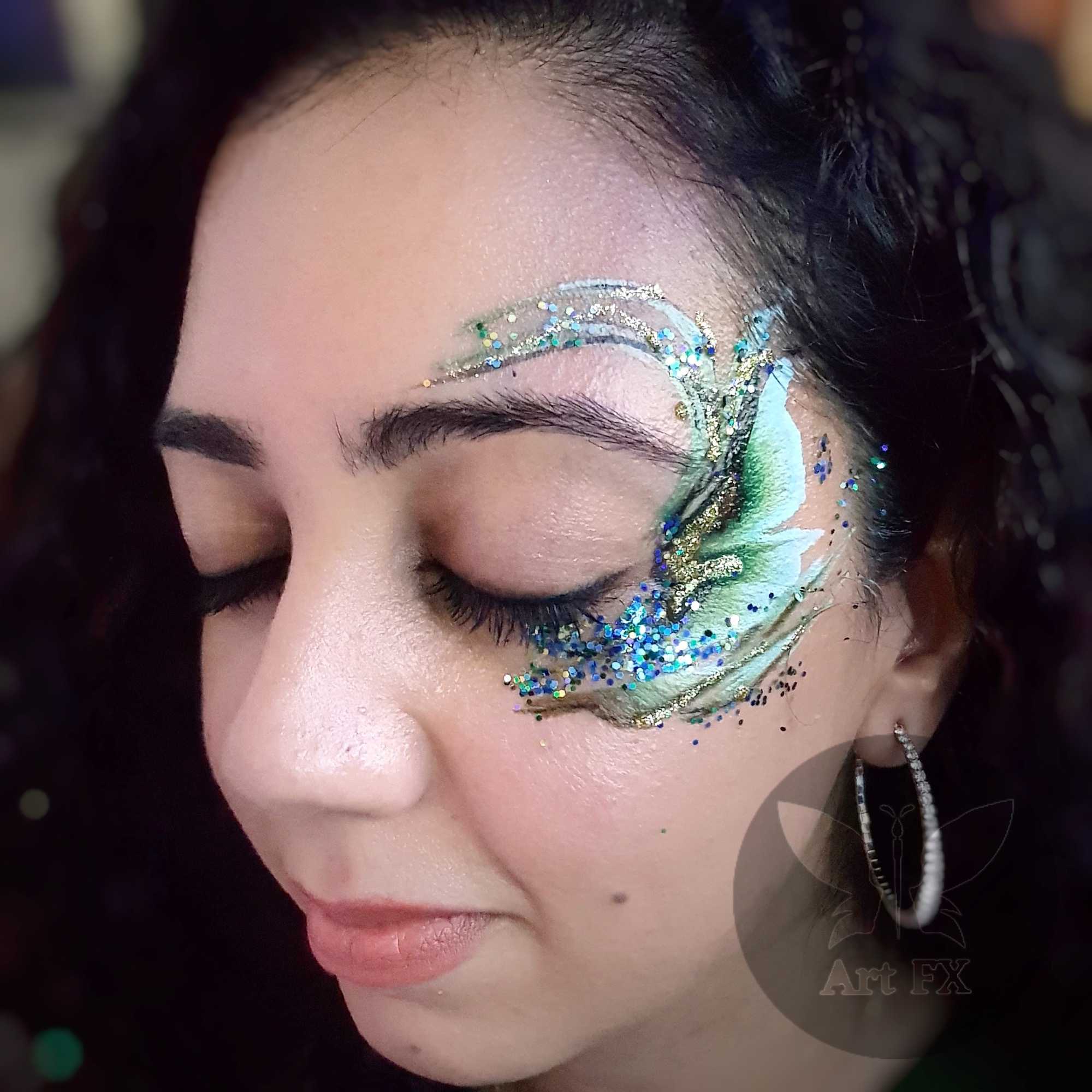A woman with a delicate white floral lace face paint design highlighted with silver chunky glitter around her eye.