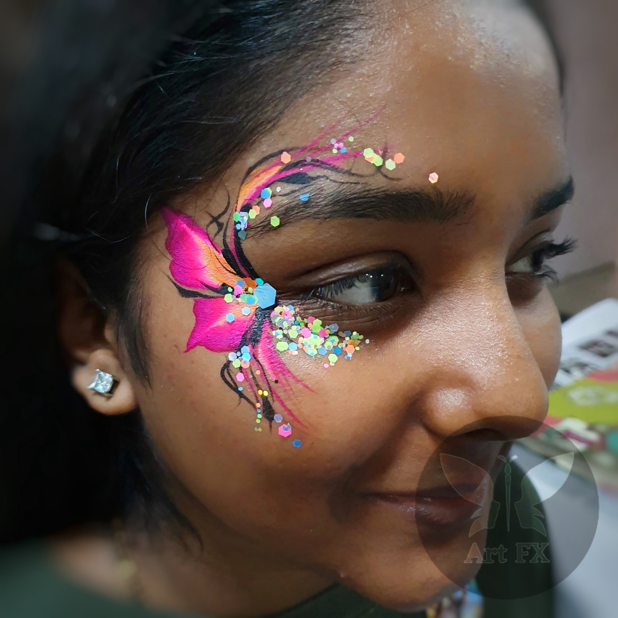 A smiling woman featuring an elegant white and pink floral face paint design with delicate details and chunky glitter.