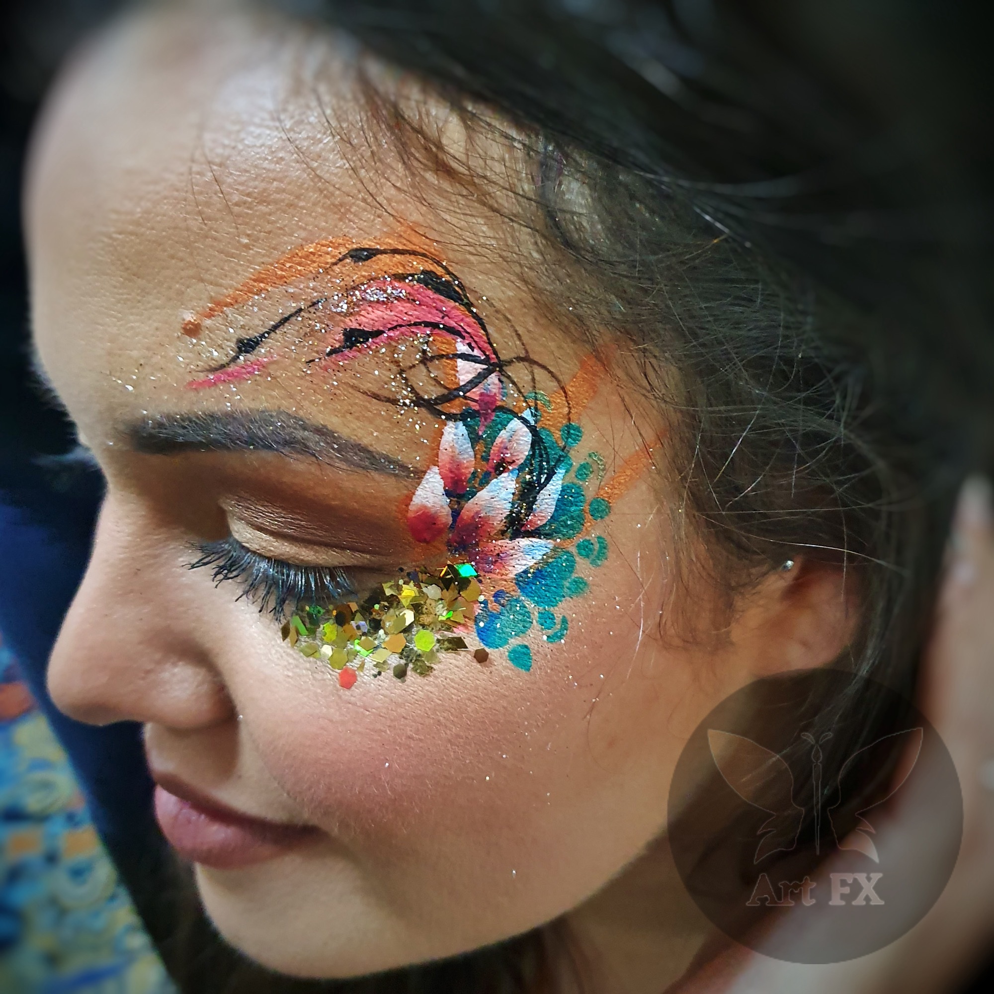 A woman with a beautiful pink and green tropical floral face paint design enhanced with silver chunky glitter.