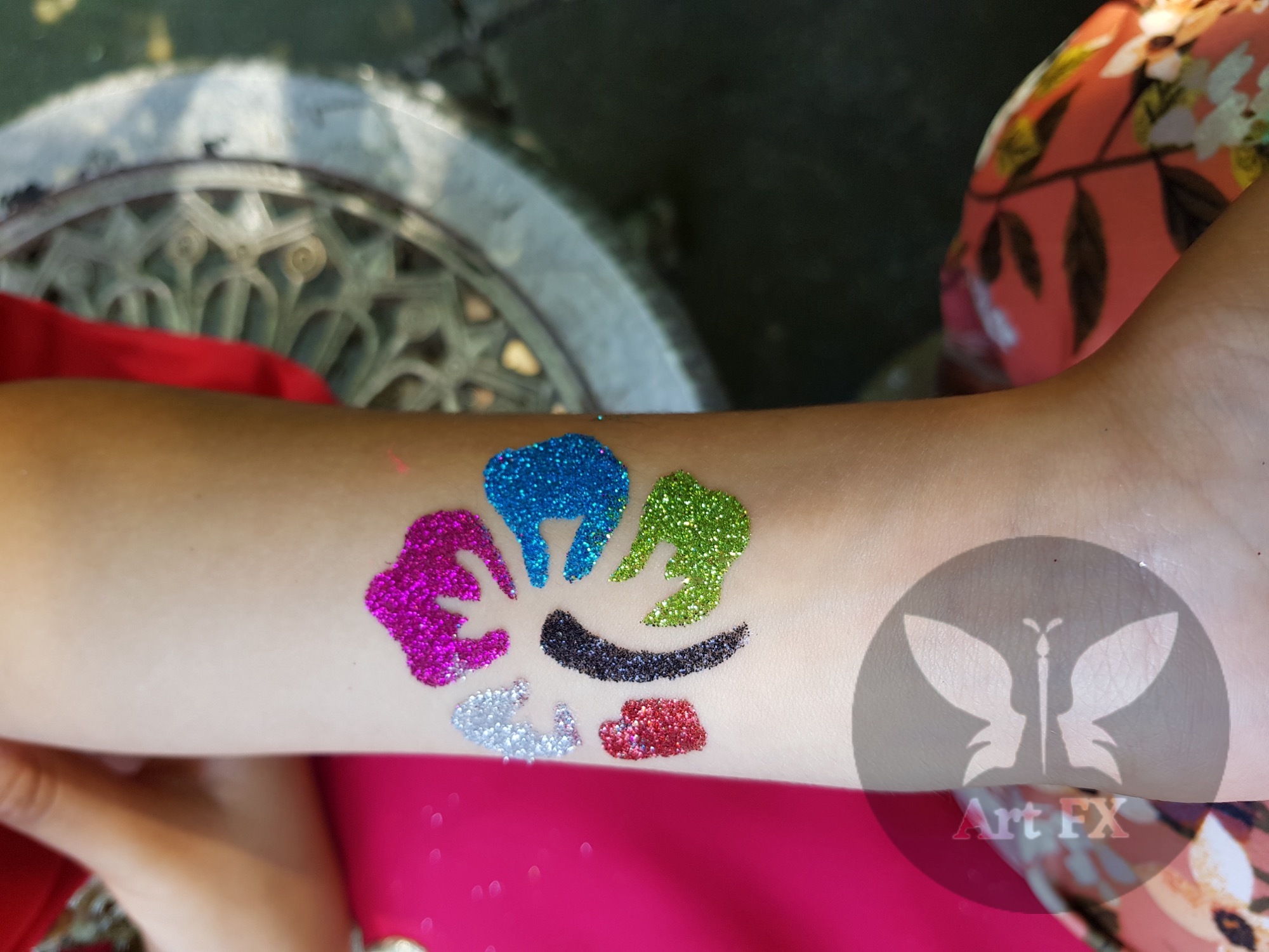 Colorful glitter tattoo of a paw print or flower pattern on an arm.
