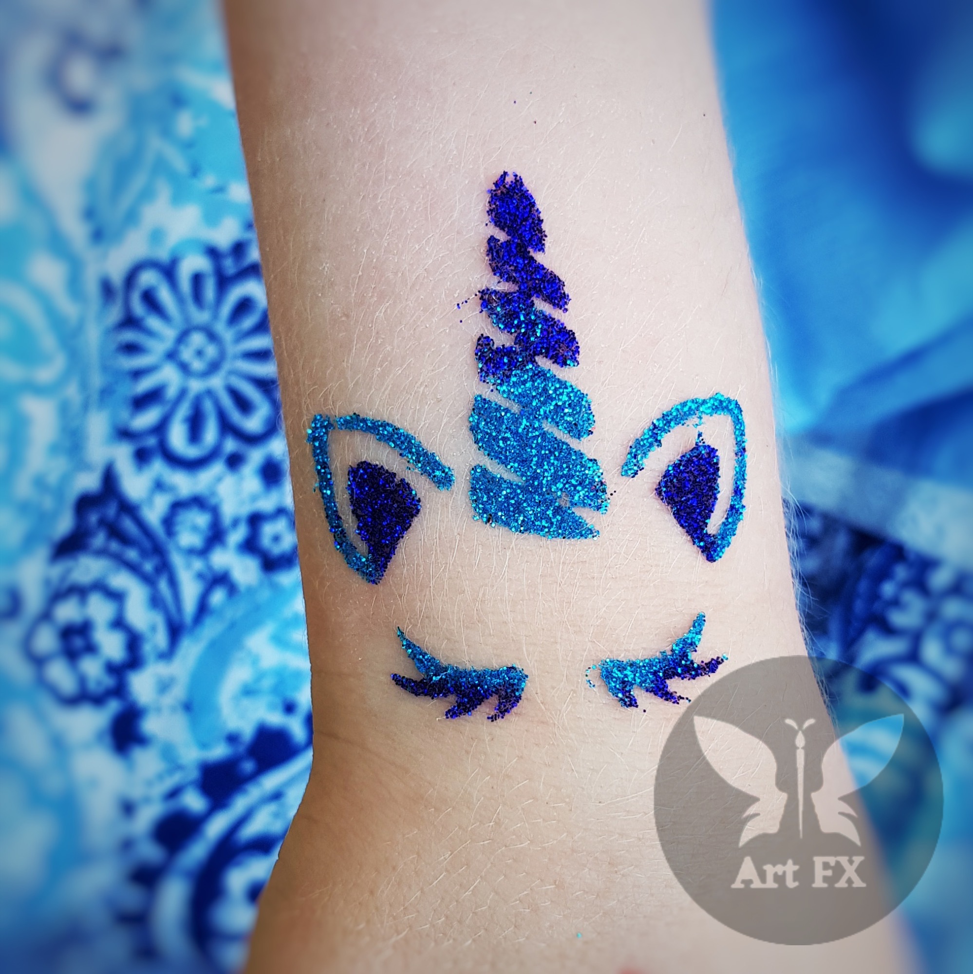Blue glitter tattoo of a unicorn's face with a sparkly horn and eyelashes.