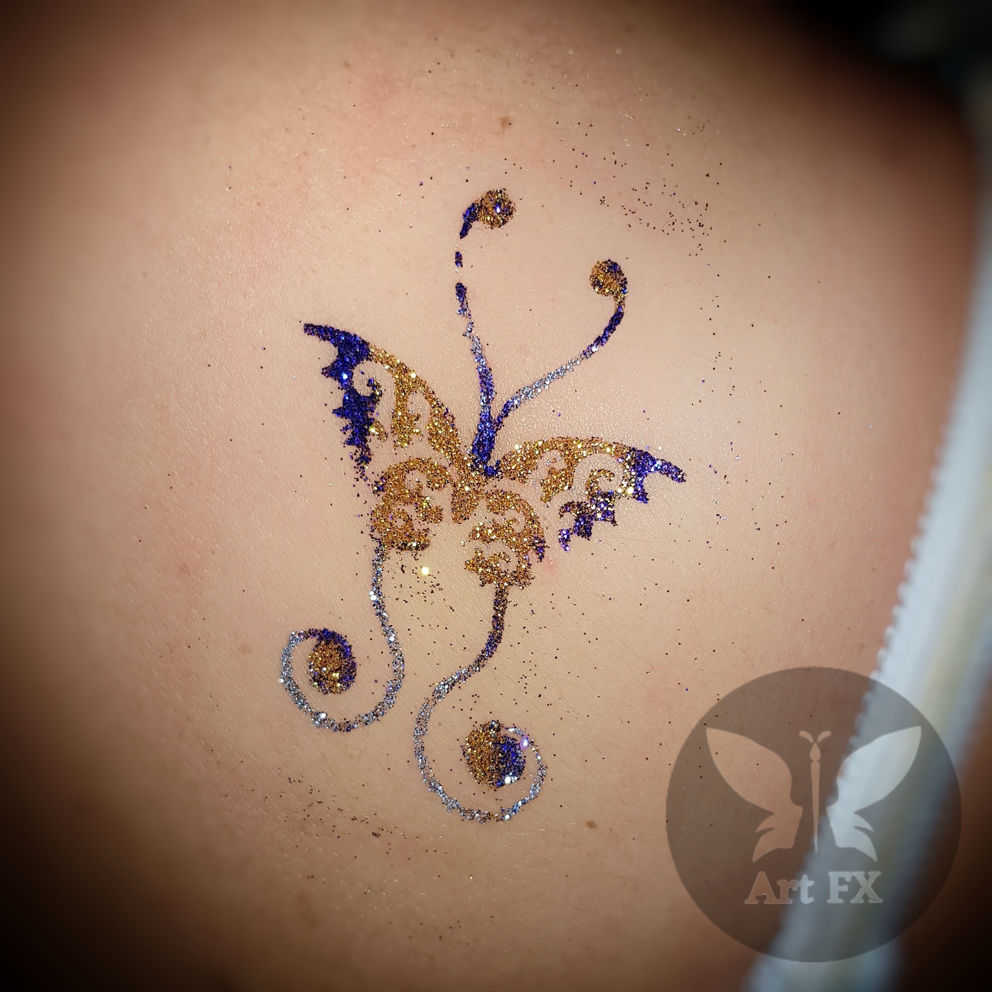 Delicate gold, silver, and blue glitter tattoo of a decorative butterfly.