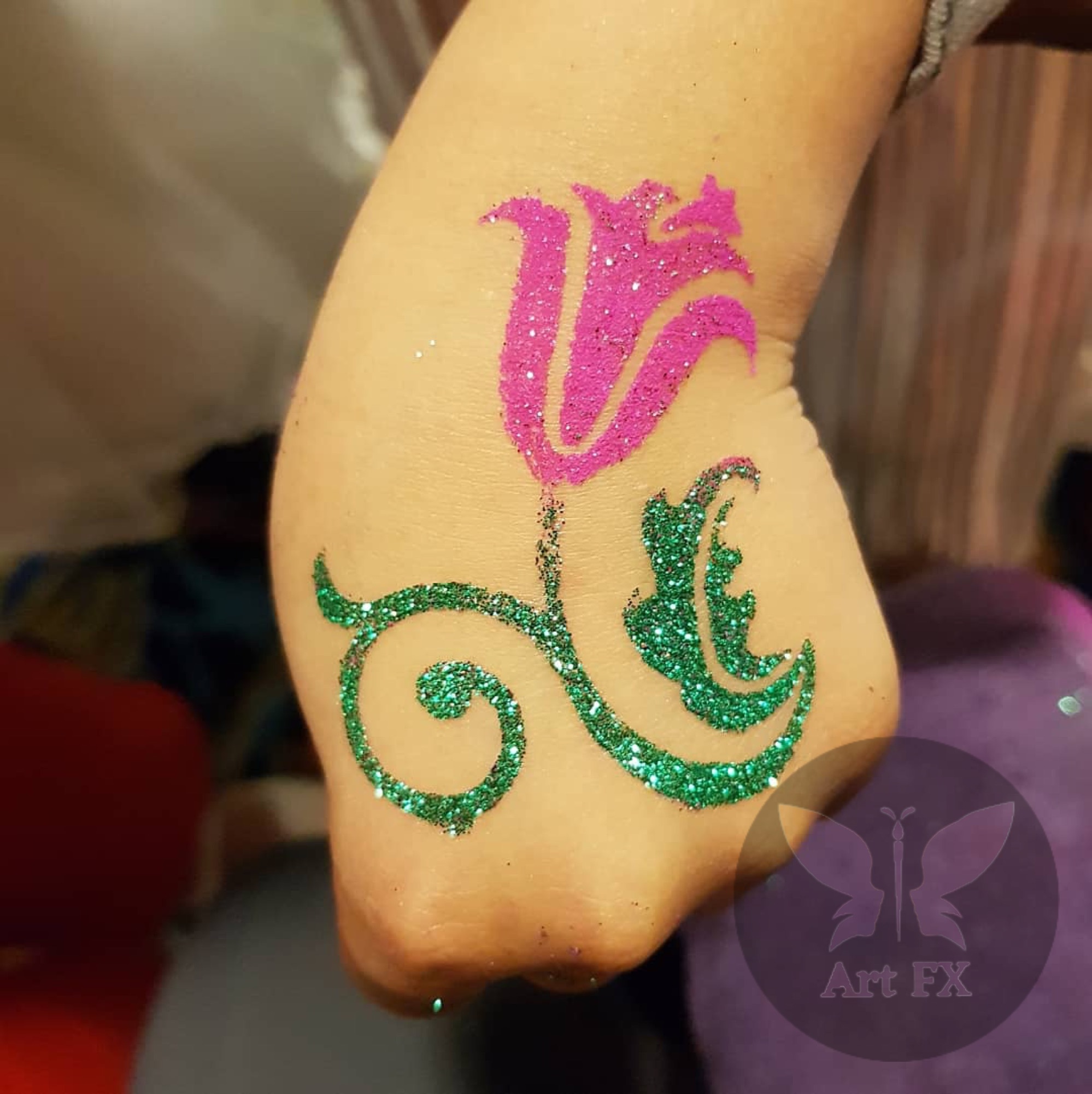 Pink tulip glitter tattoo with a green swirling stem and leaf.