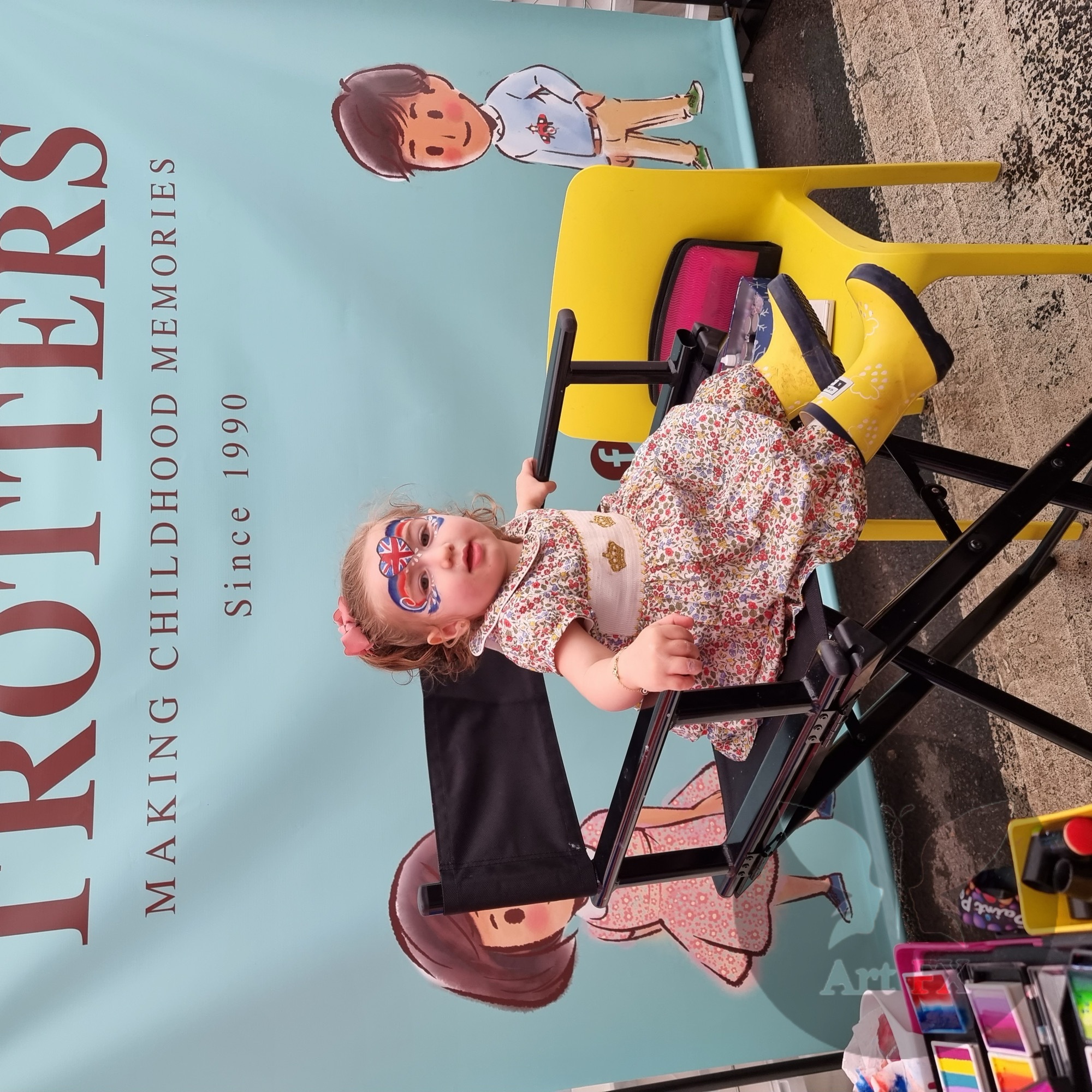 A young girl sitting in a professional makeup chair showing off her Union Jack heart face paint design.