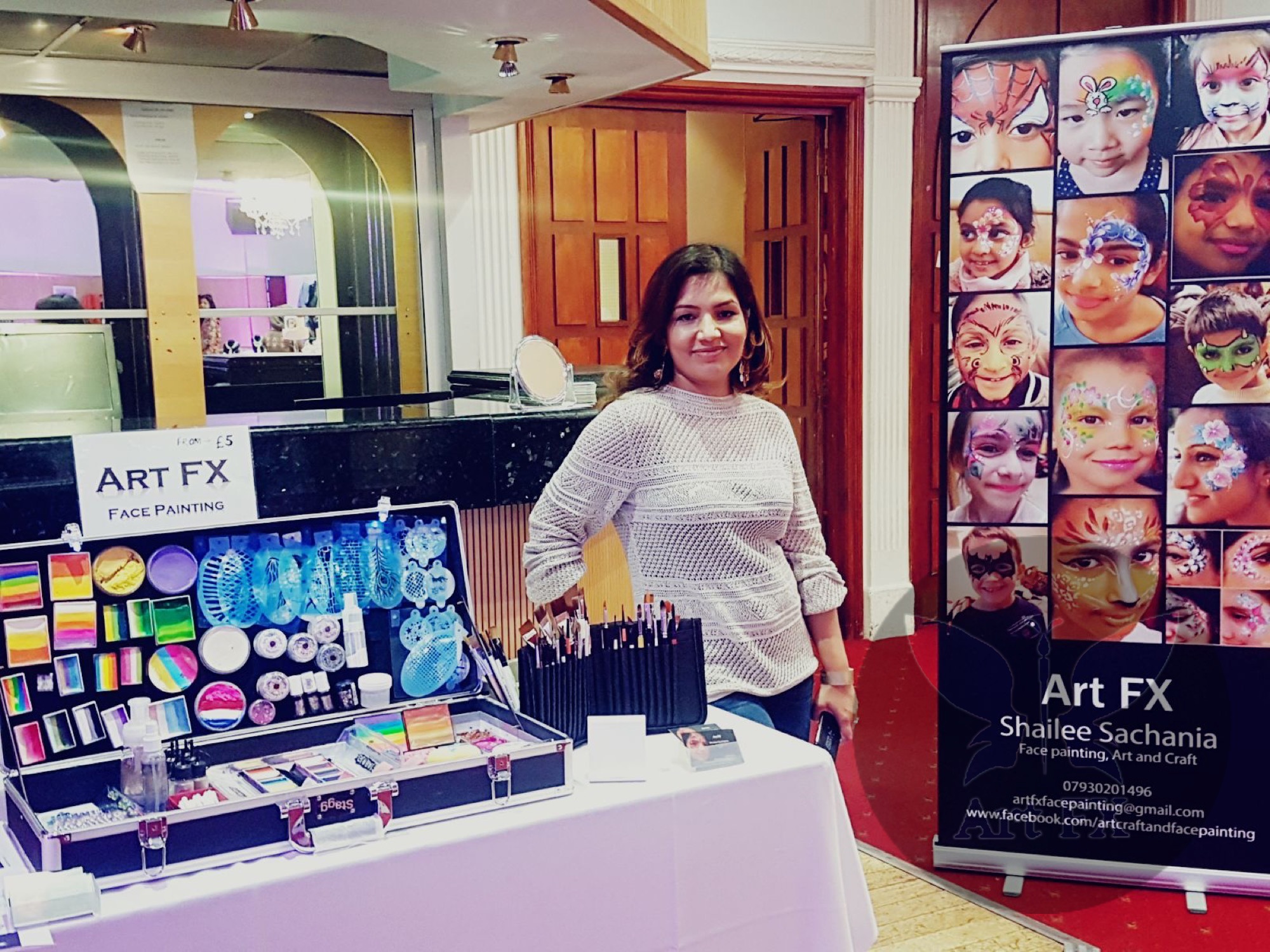 Shailee at a corporate event with her face painting station and a large banner showcasing her portfolio.