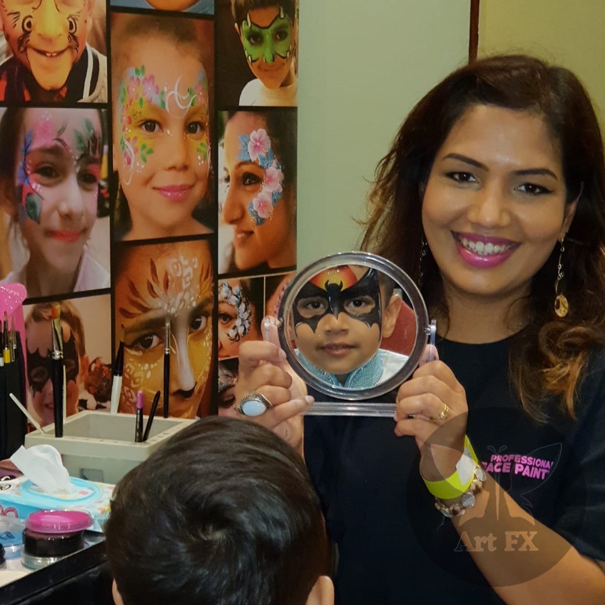 A young boy admiring his Batman face paint design in a mirror held by Shailee.