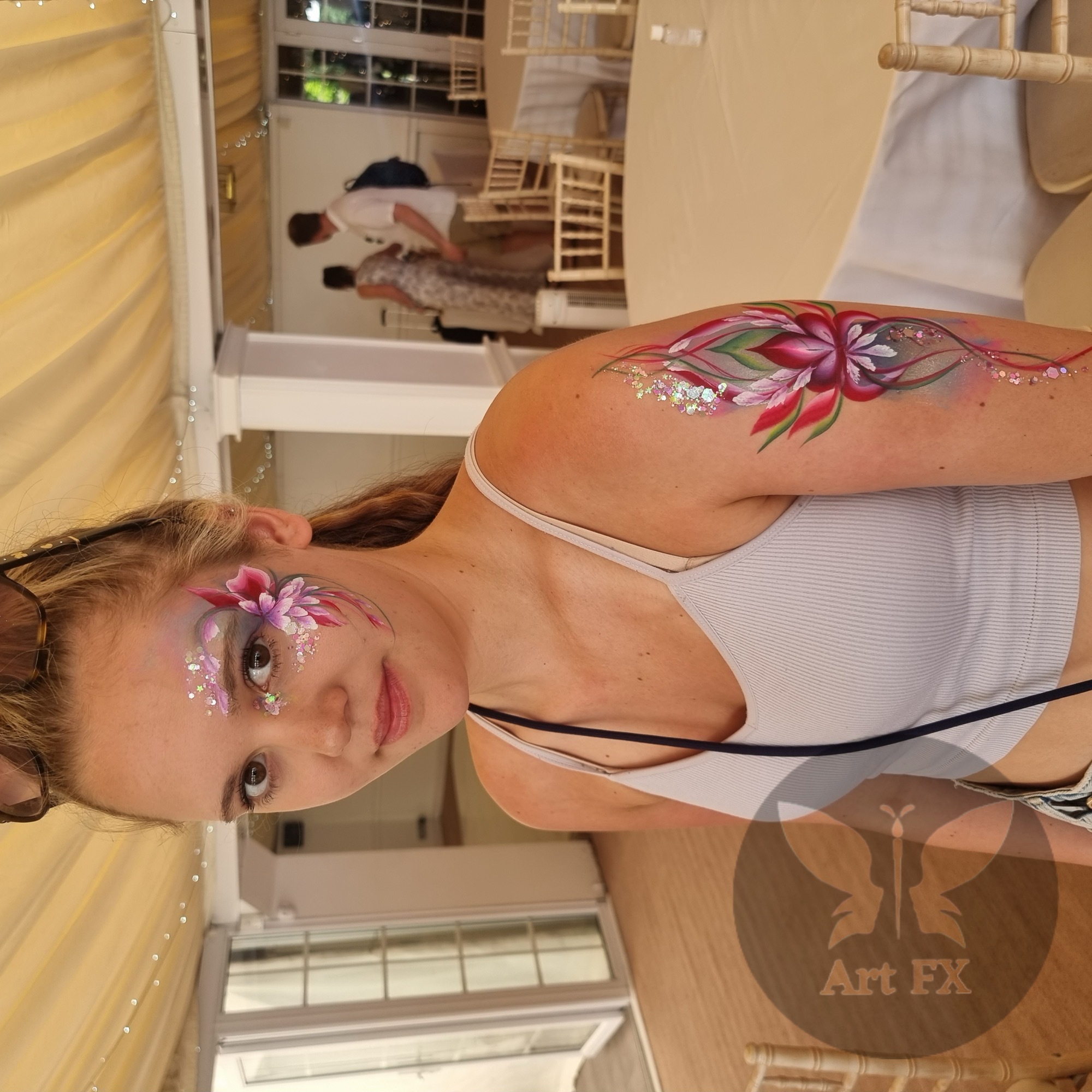 Young girl smiling with a vivid rainbow butterfly face painting design and purple teardrop accents
