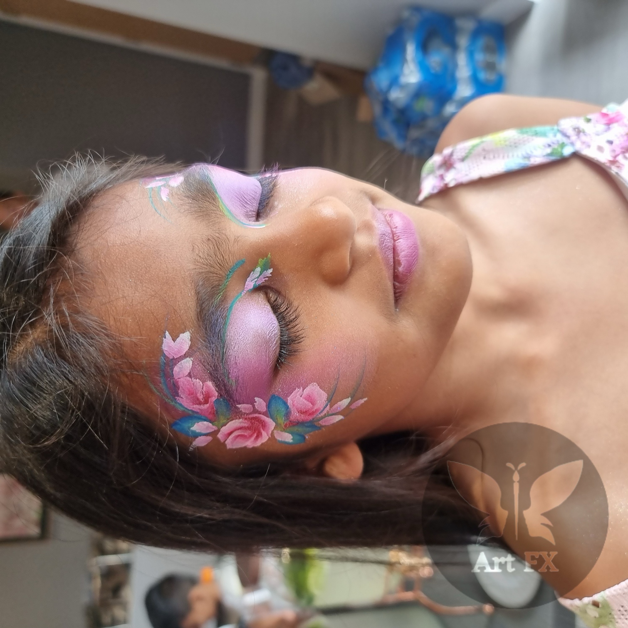 Young girl displaying a stunning pink, purple, and green floral face painting design around one eye