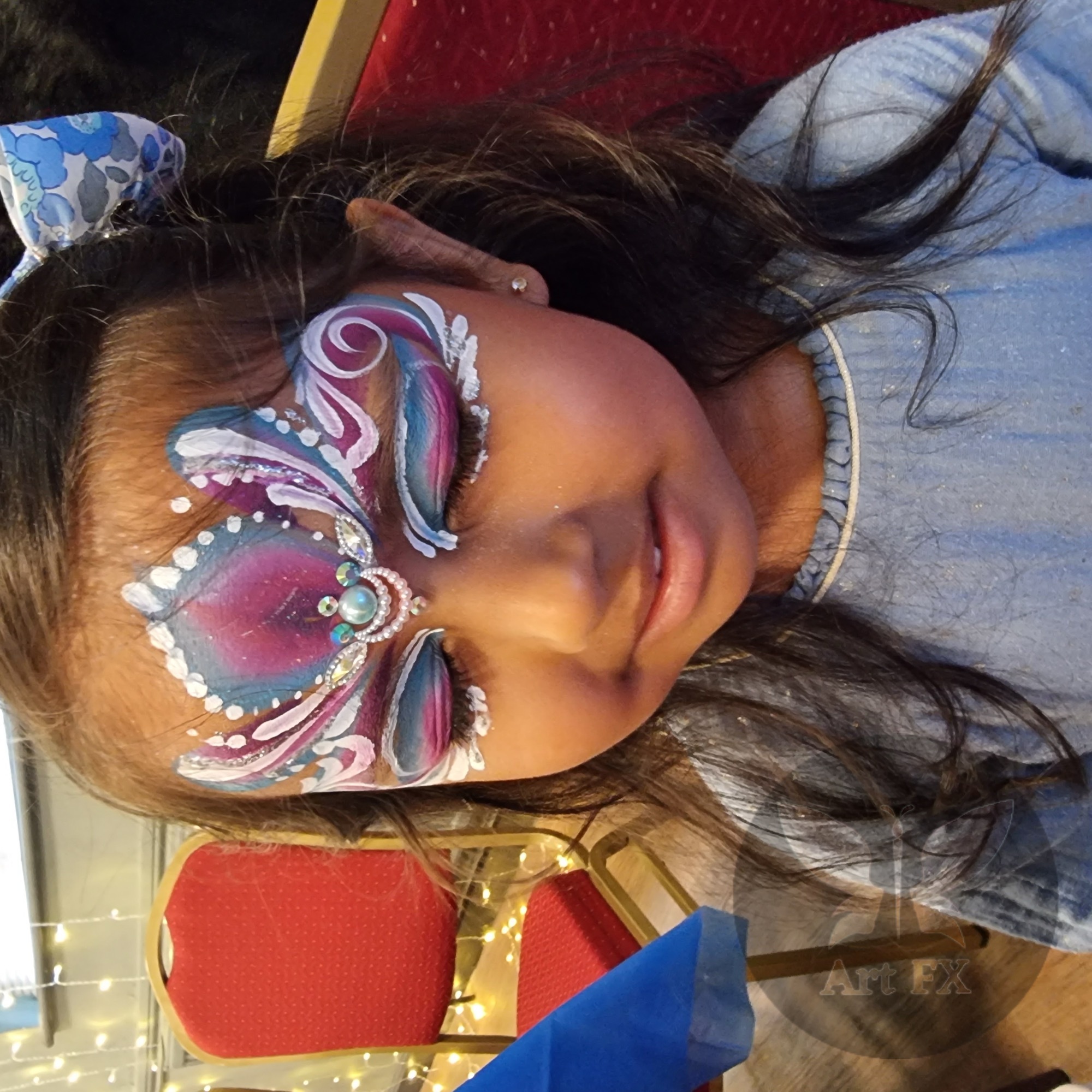 Young girl smiling with a beautiful pink and blue butterfly face painting mask design