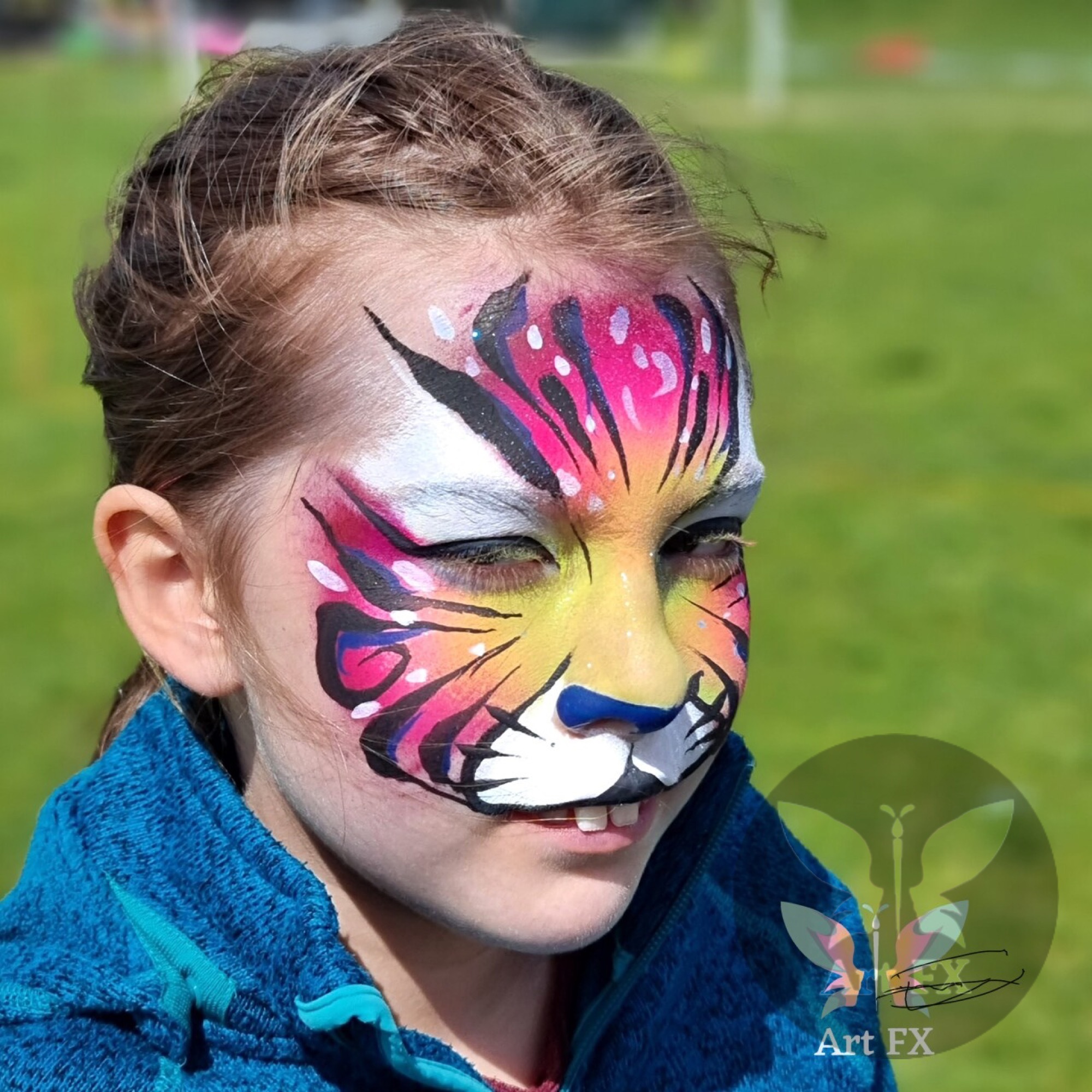 Young girl displaying an intricate pink and teal butterfly face painting mask with floral center