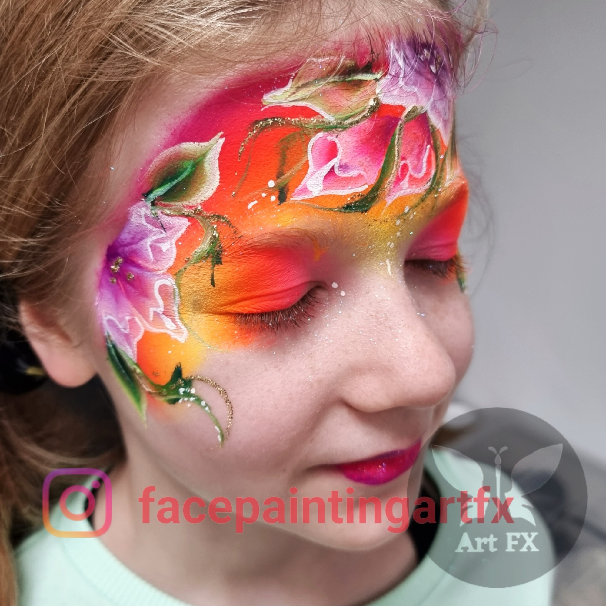 Young girl looking down with a vivid orange, pink, and purple floral face painting design featuring green leaves and vines