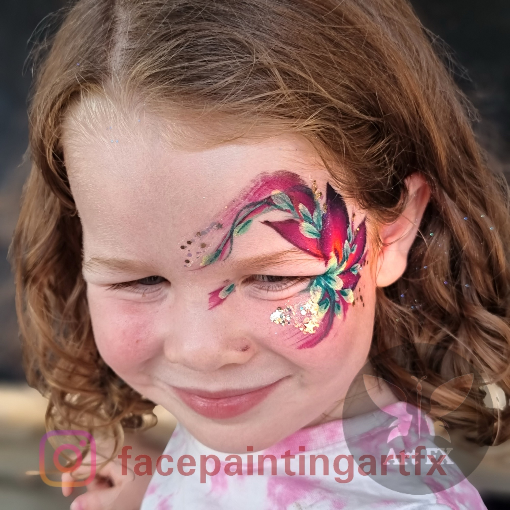 Young girl smiling softly with an elegant dark pink, red, and green floral face painting design around one eye