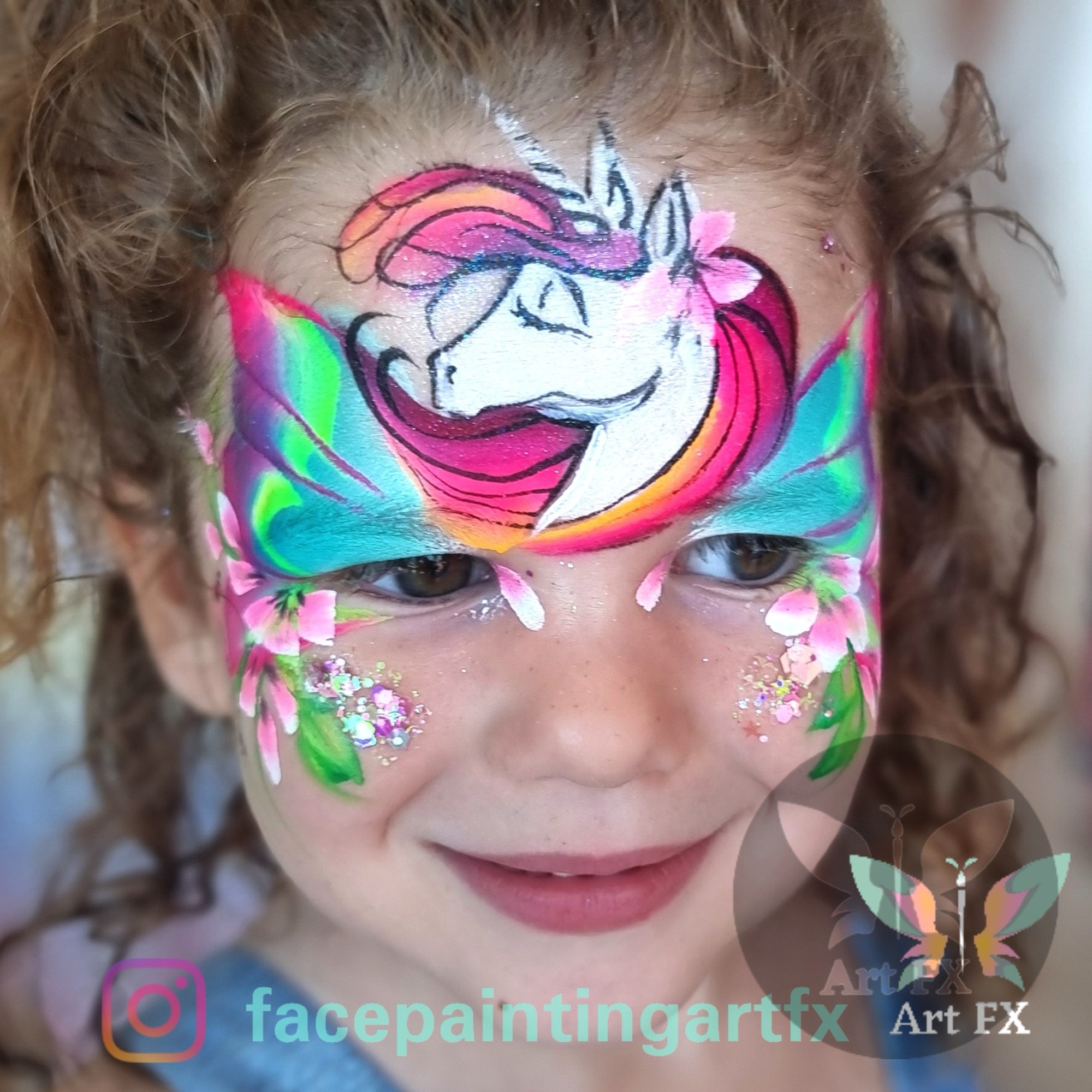 Young girl smiling featuring a magical rainbow unicorn face painting design with bright colorful butterfly wings