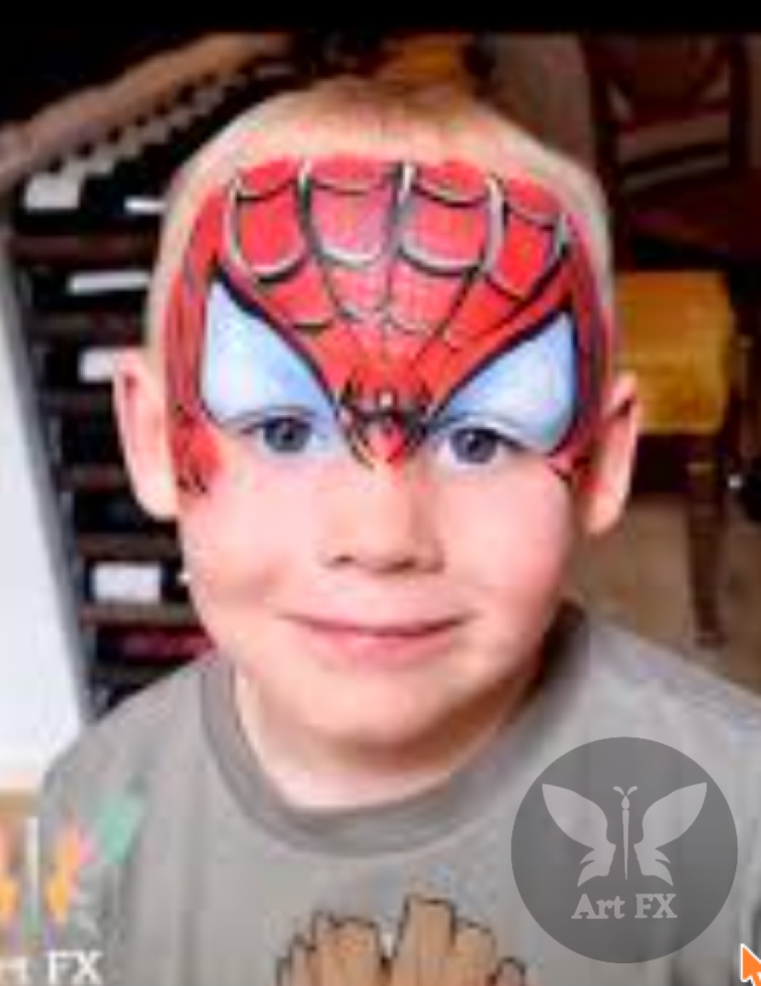 Young boy smiling displaying a classic red and black Spiderman superhero mask face painting design